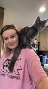 A woman holding a cat on her shoulder.