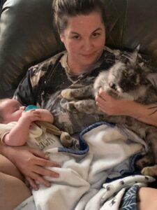 A woman holding a cat and baby in her lap.