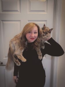 A woman holding a cat on her shoulder.