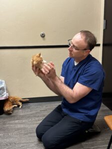 A man sitting on the floor holding an orange cat.