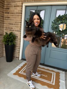 A woman holding two cats on the front porch.