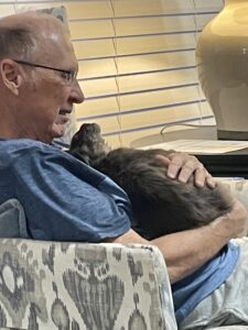 A man sitting on top of a couch with his arm around a cat.