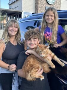 Family holding a large ginger Maine Coon cat.